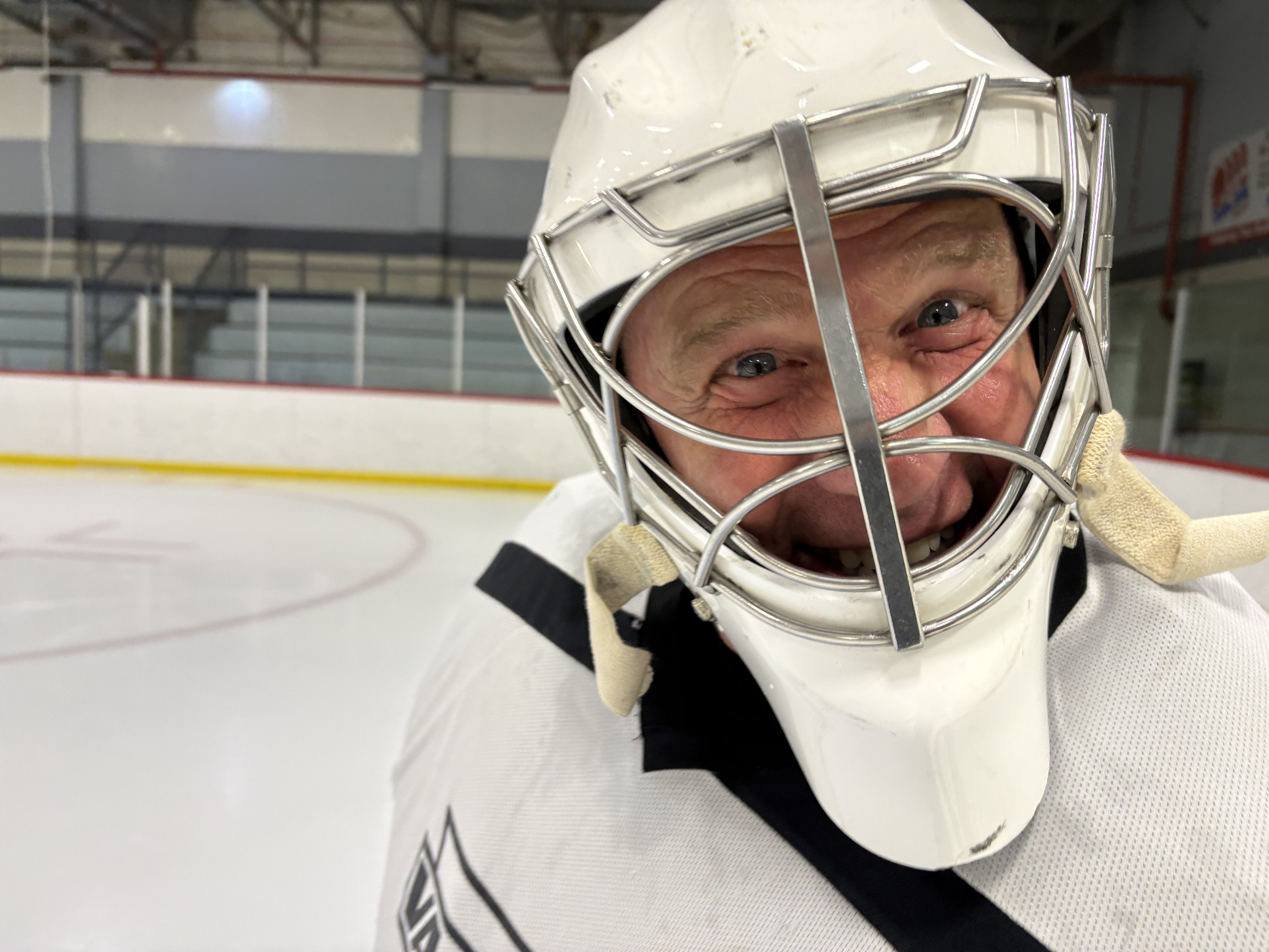 A smiling Never 2 Late Hockey goalie on the ice